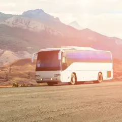 Biały autokar jedzie drogą w malowniczym, górzystym krajobrazie. Kierowca autobusu wiezie pasażerów w podróż.