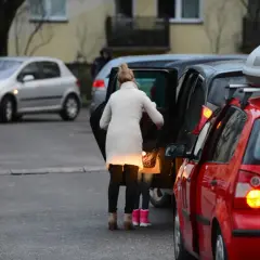 Kobieta z dzieckiem wsiada do samochodu, obok stoją inne auta.