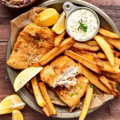 Chrupiące **fish and chips** z cytryną i sosem tatarskim na drewnianym stole. Idealna przekąska!