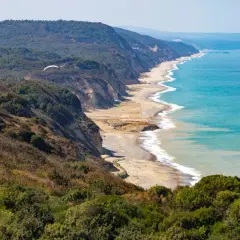 Widok na wybrzeże Karaburun z klifami, plażą i turkusowym morzem. W oddali widać paralotnię.