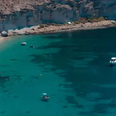 Gente disfrutando del sol y el mar en la playa de San Pedro. Barcos y motos acuáticas navegan en aguas cristalinas.