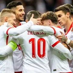 Piłkarze reprezentacji Polski w białych strojach świętują razem, przytulając się.