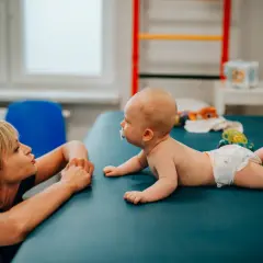 Fizjoterapeutka wspiera niemowlaka z nieprawidłowym leżeniem na brzuchu, zachęcając go do aktywności.