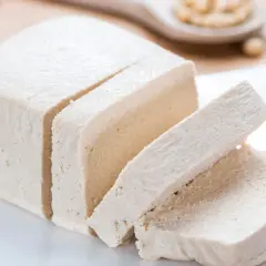 Kostka tofu, z czego jest zrobione? Z ziaren soi. Pokrojone na plastry, prezentuje swoją delikatną strukturę.