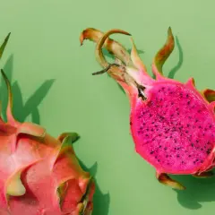 Zwei leuchtend pinke Drachenfrüchte, eine angeschnitten, zeigen ihr gesundes, kernreiches Inneres auf grünem Hintergrund.