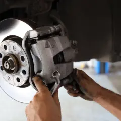 Mechanik dokręca śrubę prowadnicy z gumką góra czy dół, naprawiając hamulce samochodu.