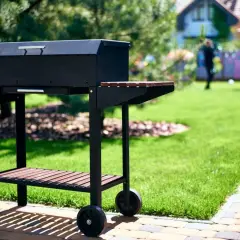 Czarny grill na kółkach w ogrodzie, gotowy na przyjęcie gości. Idealny pomysł na to, co na grilla tanio i smacznie.