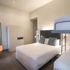Habitación familiar en Petit Palace Canalejas Sevilla con cama doble, litera y sillón naranja.
