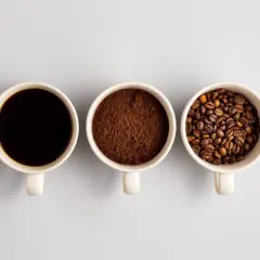 Tre tazze mostrano il viaggio del caffè: chicchi tostati, macinato e bevanda scura. Un'idea di da dove proviene il caffè.