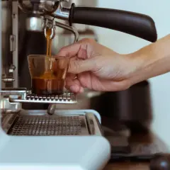 Eine Hand hält ein Glas, während frisch gebrühter Espresso manuell zubereitet wird.
