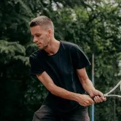 Mężczyzna w czarnej koszulce uderza rakietą piłkę tenisową. To właśnie o co chodzi w tenisie – precyzja i dynamika.