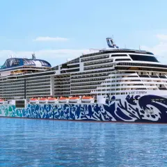 Rejsy po fiordach norweskich z Polski statkiem MSC Euribia. Ogromny statek wycieczkowy z niebieskimi zdobieniami na kadłubie płynie po spokojnym morzu.