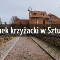 Kamienny most prowadzi do ceglanego zamku krzyżackiego w Sztumie. W oddali widać drzewa i pochmurne niebo.
