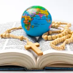 Na otwartej Biblii leży globus, różaniec i drewniany krzyż. To symbol wiary, która obejmuje cały świat, jak wdowi grosz ofiarowany z serca.
