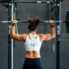 Femme musclée en tenue de sport, soulevant une barre chargée. Elle s'entraîne pour un superset musculation, concentrée sur sa performance.