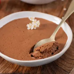Une cuillère prend une bouchée d'une mousse au chocolat au lait aérienne, décorée de petites fleurs blanches.
