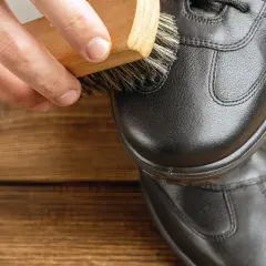 Brosse en bois appliquant un produit sur une chaussure en cuir noir. Pour imperméabiliser chaussures avant ou après cirage, un bon entretien est essentiel.