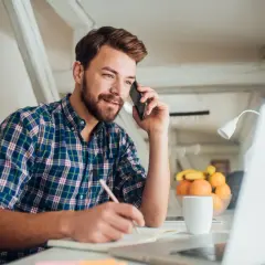 Mężczyzna rozmawia przez telefon, notuje i pracuje przy laptopie. To dobry moment, by zastanowić się, kiedy najlepiej szukać pracy.