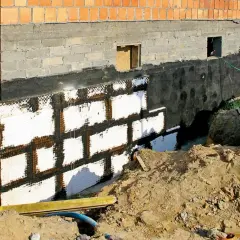 Nowe ściany w piwnicy z izolacją i siatką. Budowa fundamentów domu.