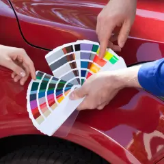 Due mani scelgono la vernice auto che cambia colore, confrontando campioni su un'auto rossa lucida.