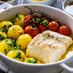 Pyszna pieczona ryba z ziemniakami i pomidorkami koktajlowymi, skropiona oliwą i posypana ziołami.