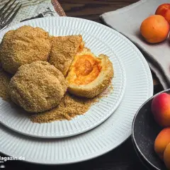 Mehlspeisen aus Kartoffelteig mit Aprikosenfüllung, paniert und auf einem Teller mit zerbröselten Semmelbröseln angerichtet. Daneben frische Aprikosen.