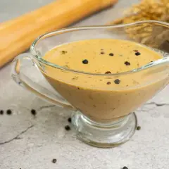Salsa a la pimienta cremosa en una salsera de cristal, con granos de pimienta negra esparcidos.