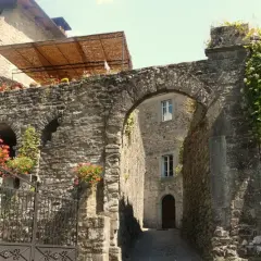 Un vicolo suggestivo a Casola in Lunigiana, con un arco in pietra, fiori rossi e edera rampicante.