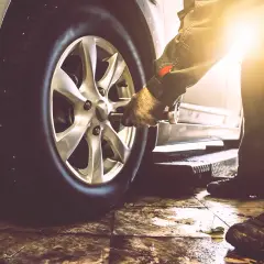 Mechanik w rękawicy używa klucza do odkręcenia koła samochodu. Pokazane jest, jak odkrecic kolo.
