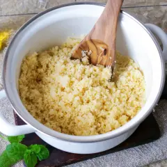 Frisch zubereiteter Couscous in einem Topf, bereit zum Servieren. Ein Holzlöffel lockert die Körner auf. Öl und Minze deuten auf die Couscous Zubereitung hin.