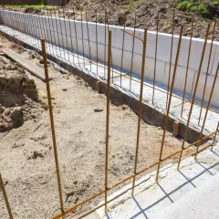 Zbrojenie schodów na budowie: pionowe i poziome pręty stalowe w wykopie.