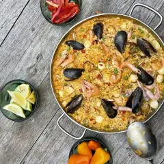 Ein köstliches Paella-Rezept mit Garnelen, Muscheln und Reis, garniert mit Zitronenspalten und Paprika.