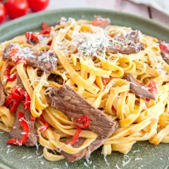 Herzhaftes Gericht mit Pasta und zarten Rinderfiletstreifen, garniert mit geriebenem Parmesan und roten Paprikastücken.