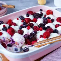Ein cremiges Windbeutel-Dessert mit frischen Beeren wie Himbeeren, Blaubeeren und Brombeeren in einer rosa Schale.