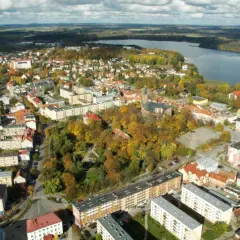 Widok z lotu ptaka na miasto z jeziorem w tle. Widać zabudowania, drzewa w jesiennych barwach i kościół. To największy rynek w Polsce.