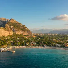 Vista aerea del mare di Palermo con la costa, la spiaggia affollata e le montagne sullo sfondo.
