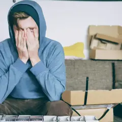 Zrozpaczony mężczyzna w bluzie z kapturem, z dłońmi na twarzy. Czy kochanek tęskni po rozstaniu?