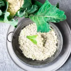 Färdigt blomkålsris i en metallskål, redo för ett hälsosamt blomkålsris recept. En del av ett blomkålshuvud syns ovanför.