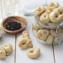 Taralli que es: crujientes bocaditos horneados, algunos en un frasco, con granos de pimienta y hinojo cerca.