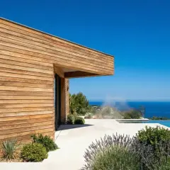 Maison moderne avec bardage bois, piscine à débordement et vue mer. Le choix du bois pour ossature bois est crucial pour ce style.