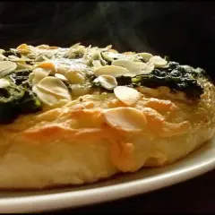 Eine köstliche Spinat Pizza mit knusprigem Teig und gerösteten Mandelblättchen. Dampf steigt auf und verspricht ein warmes, herzhaftes Gericht.