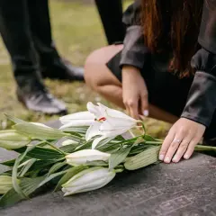 Smutek na cmentarzu. Białe lilie na nagrobku, dłoń z obrączką. Czy przesądy o śmierci w niedzielę mają sens?