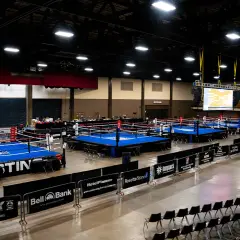Multiple boxing rings are set up in an arena, ready for competition. A large screen displays a bracket, hinting at the usa boxing weight classes.