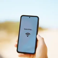Dłoń trzyma smartfon z napisem "Searching..." i ikoną Wi-Fi na tle drogi.