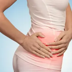 Kobieta trzyma się za bolące talerze biodrowe, zaznaczone czerwonym rumieńcem.