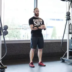 Mężczyzna z brodą wykonuje ćwiczenie pallof press przy użyciu wyciągu.