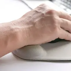Dłoń na podkładce pod mysz, zapobiegającej syndromowi myszki komputerowej.