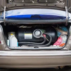 Bagażnik samochodu z zamontowanym zbiornikiem na gaz CNG. Obok kanister i torby z zakupami.