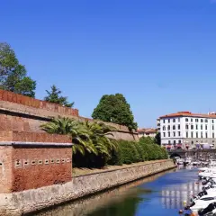 Canal bordé de bateaux à Livourne, Italie, avec une ancienne muraille de briques et des palmiers.