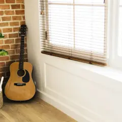 Akustyczna gitara obok ceglanej ściany i rośliny w koszu. Idealne miejsce na proste piosenki na gitarę dla dzieci.